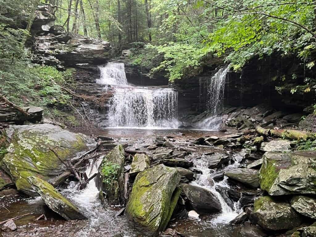 R. B. Ricketts Falls in Ricketts Glen State Park, where multiple cascades spill over a broad rock ledge into a rocky stream below.