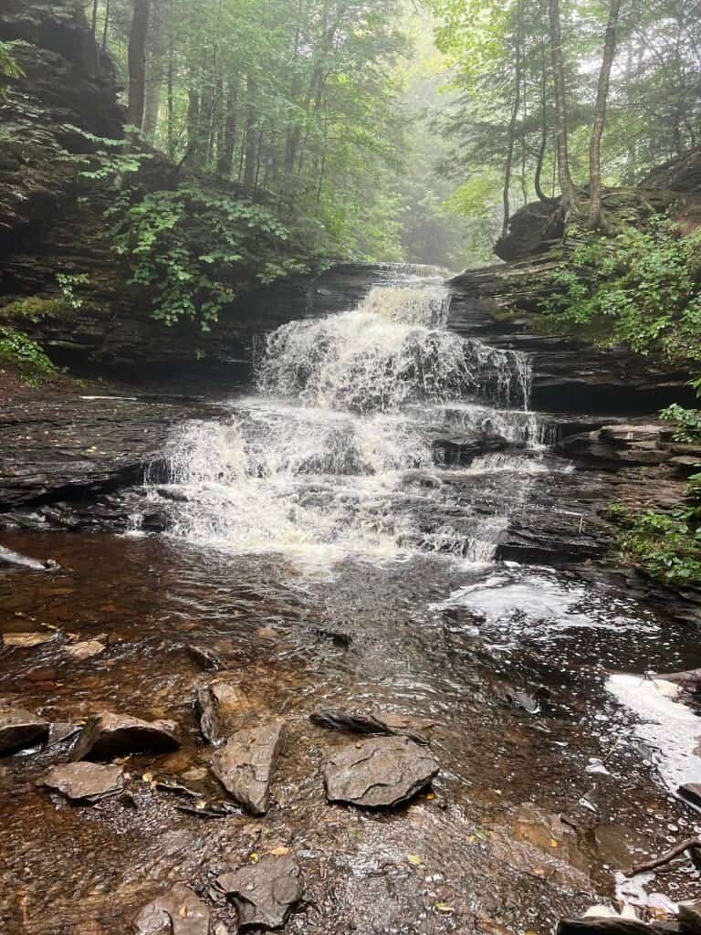 Onondaga Falls flowing over wide, stepped rock ledges into a shallow pool along the Falls Trail in Ricketts Glen State Park.