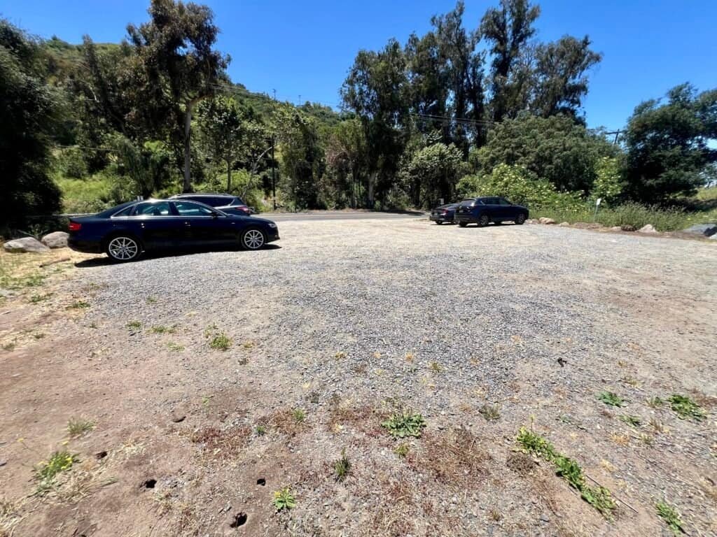 Gravel parking lot at the McGinty Mountain trailhead with several cars parked beside trees and rolling hills.