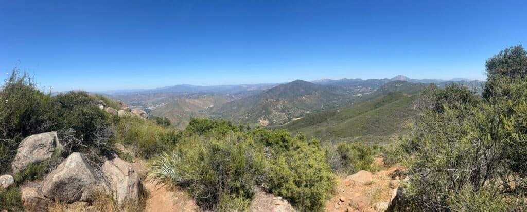 Panoramic view from the summit of McGinty Mountain showing green valleys, winding trails, and distant mountain ranges.