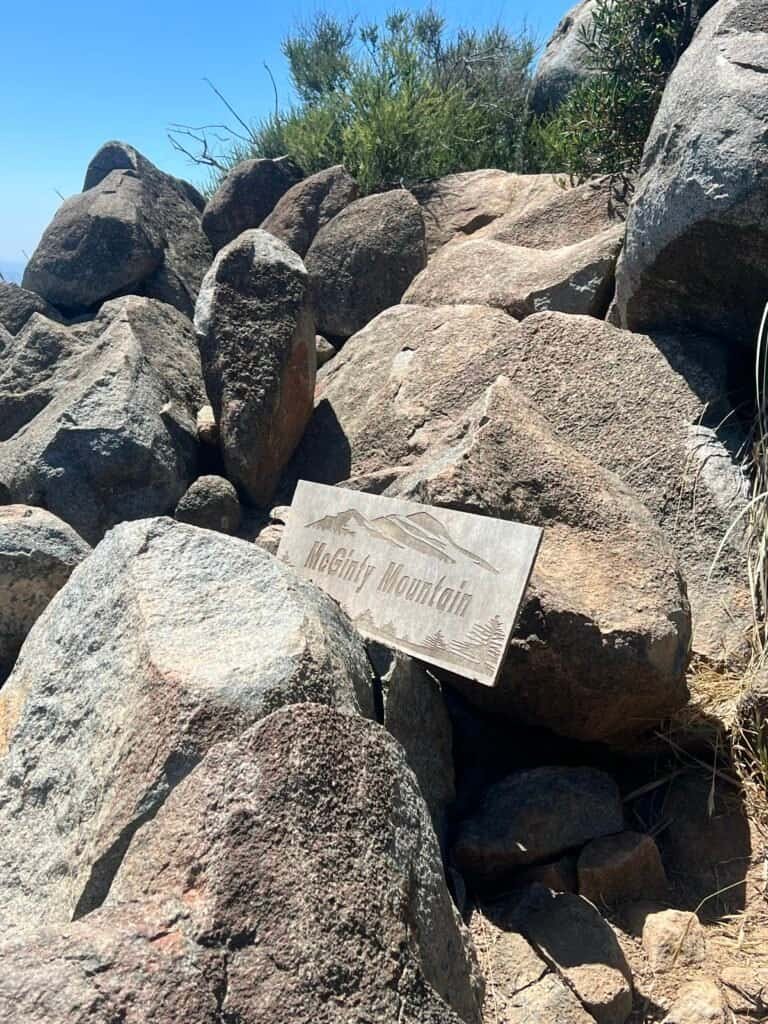 Wooden McGinty Mountain summit sign tucked among large rocks at the top of the trail.
