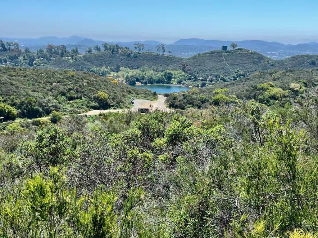 View overlooking Dixon Lake from Creek Crossing Trail at Daley Ranch, with rolling hills and distant mountains.