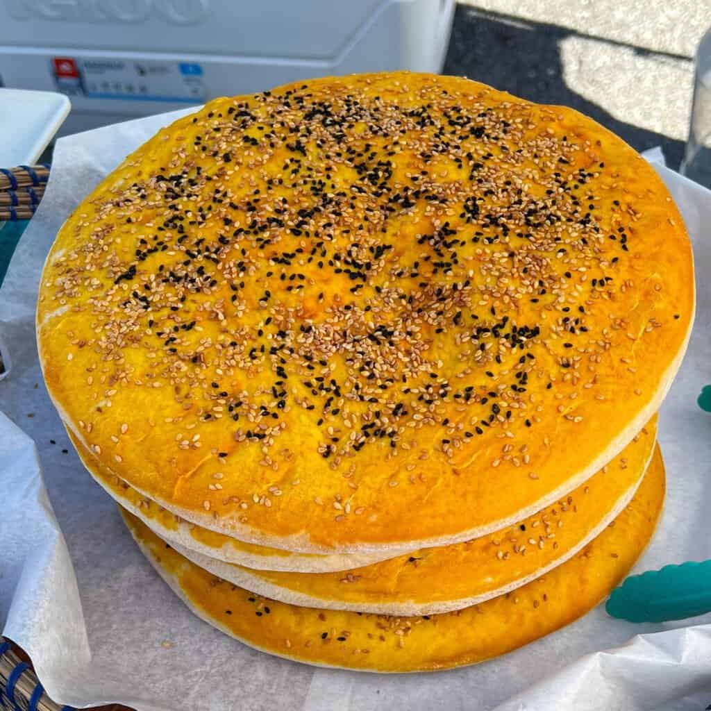 Stack of freshly baked Persian sun bread topped with sesame and nigella seeds displayed at the Lexington, Virginia farmers market.