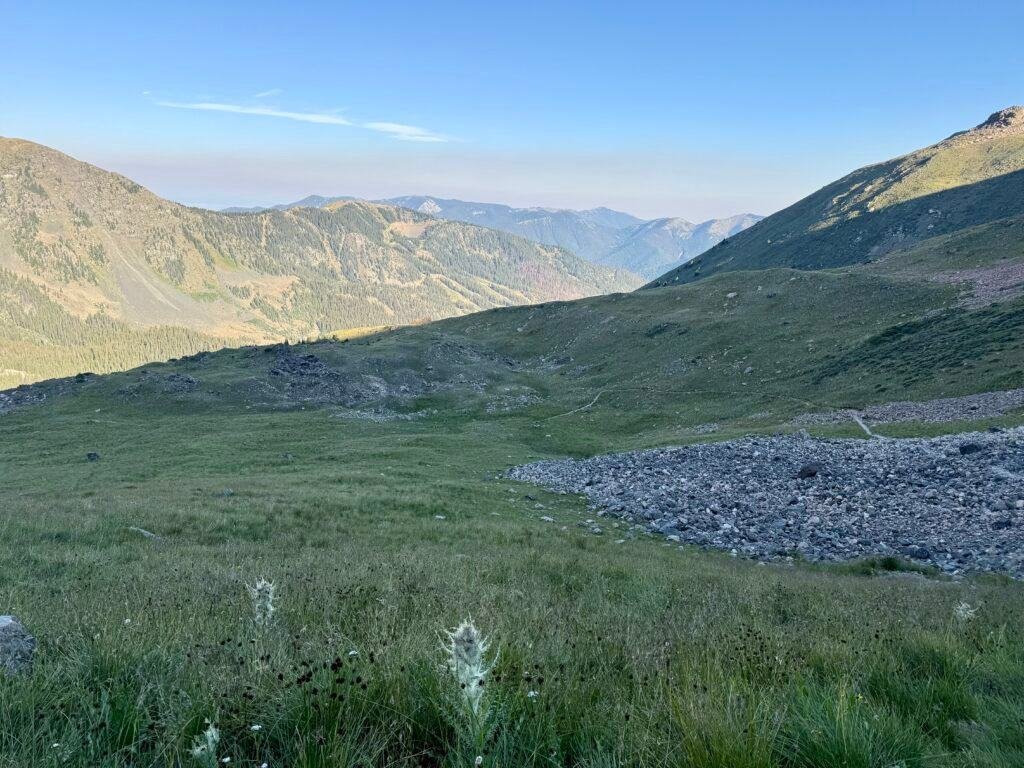 Alpine basin and distant ridgelines below the Wheeler Peak trail, showing the long descent and exposed terrain above treeline.