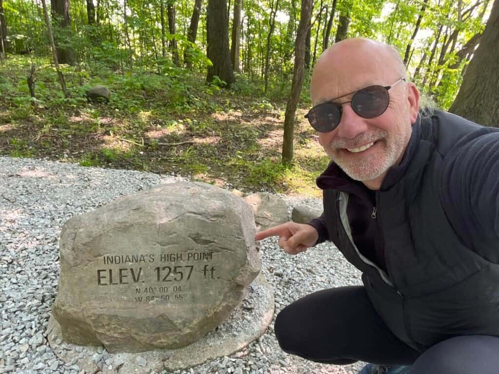 Visitor at Hoosier Hill standing next to Indiana’s high point marker at 1,257 feet
