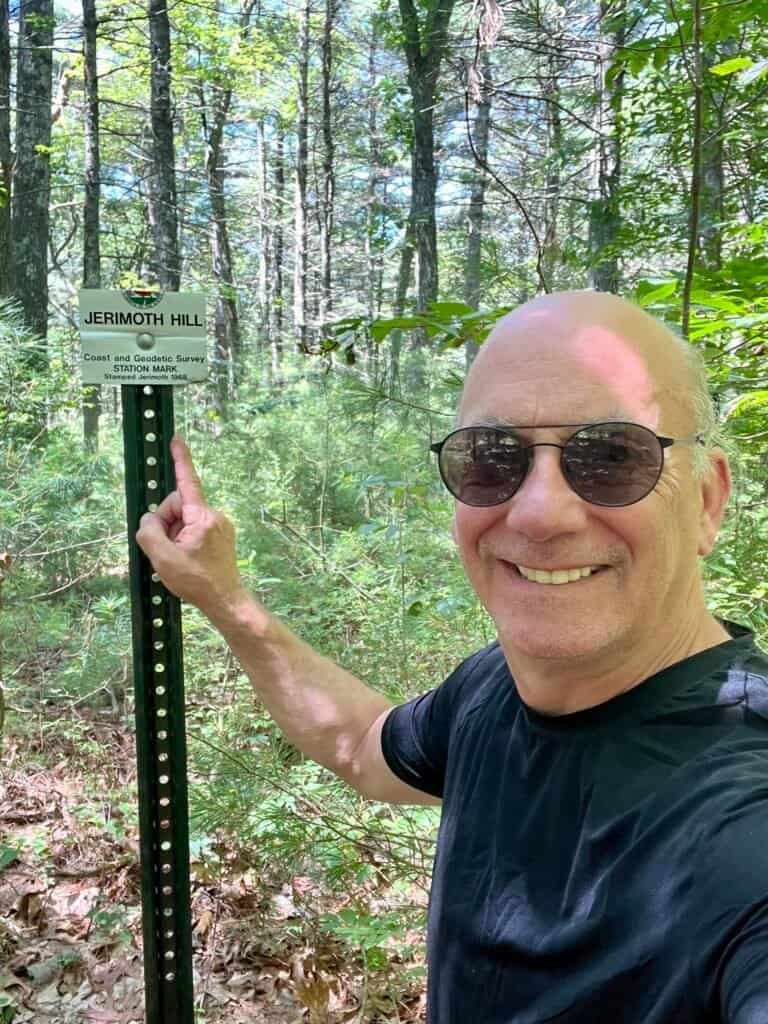 Hiker posing next to the Jerimoth Hill summit marker in Rhode Island