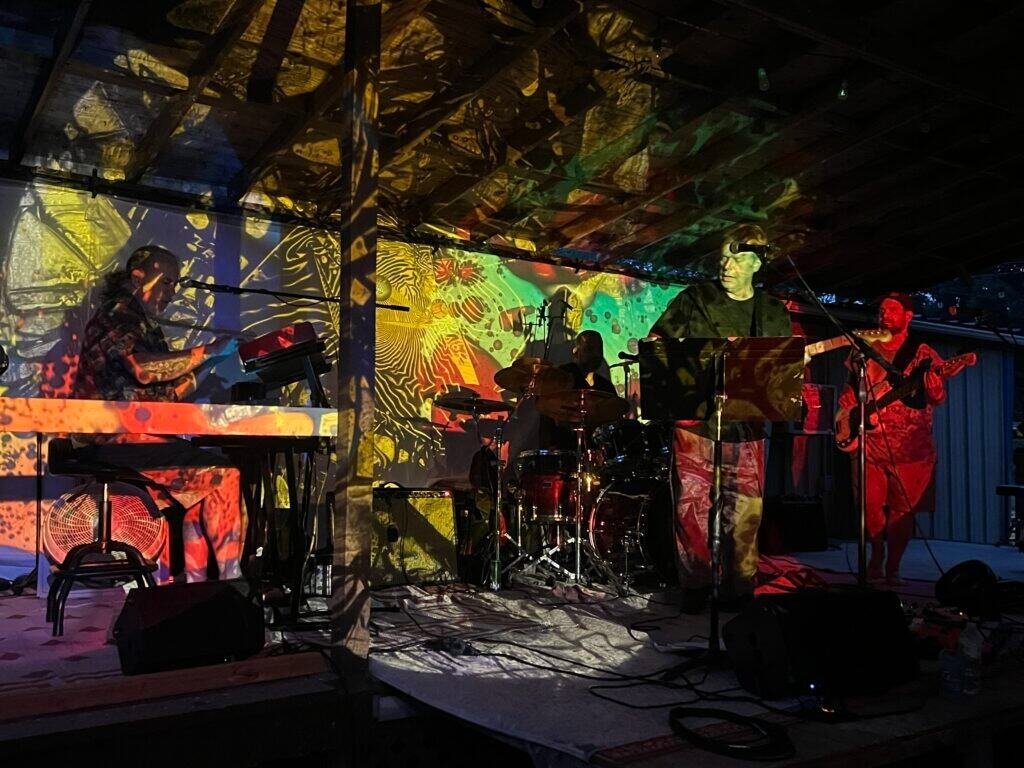 Grateful Dead tribute band performing on an outdoor stage with colorful psychedelic light projections