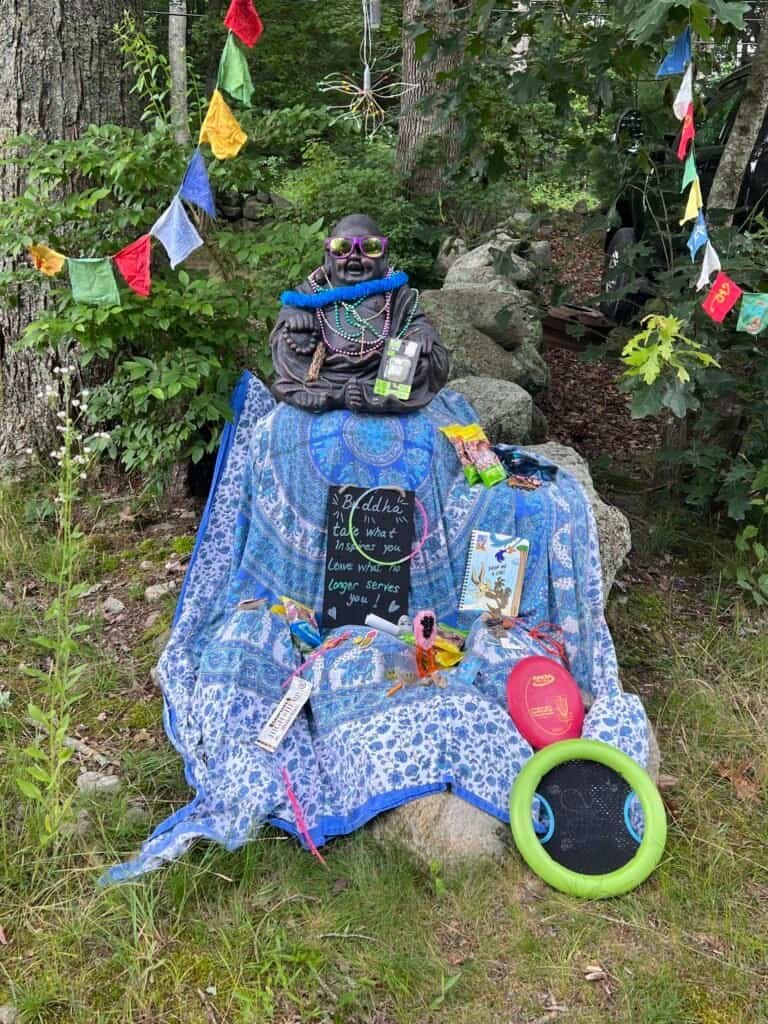 Decorated Buddha statue surrounded by colorful flags and small offerings at a campground