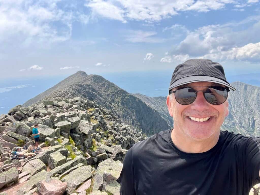 Hiker smiling at the summit of Mount Katahdin with Knife Edge in background