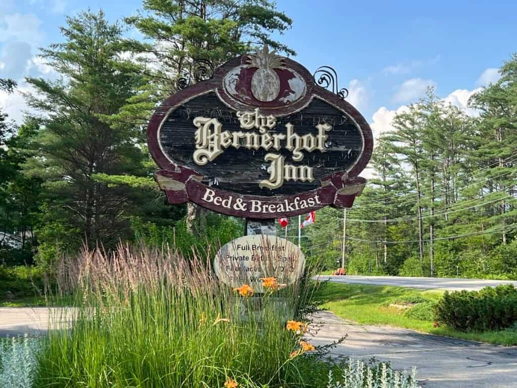 Wooden roadside sign for the Bernerhof Inn Bed & Breakfast surrounded by trees and summer landscaping in Glen, New Hampshire.