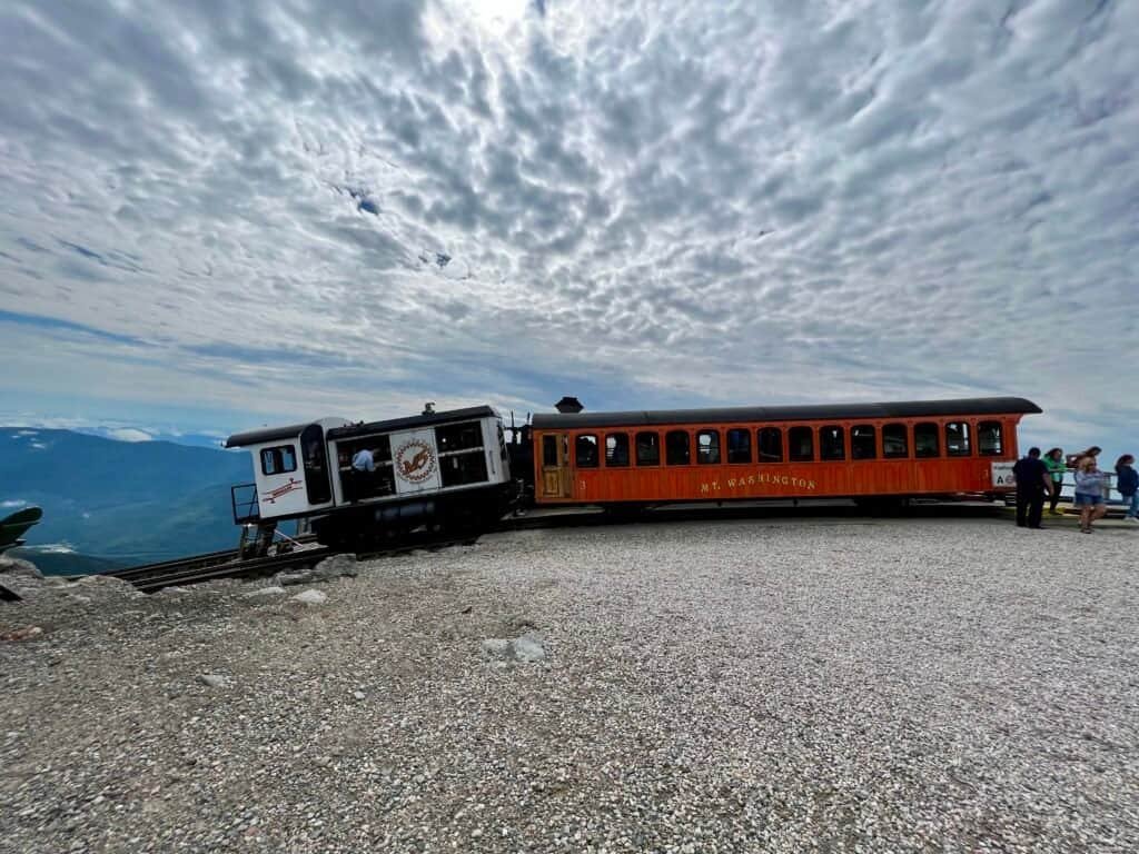 Mount Washington Cog Railway train stopped at the summit of Mount Washington under dramatic cloud cover.