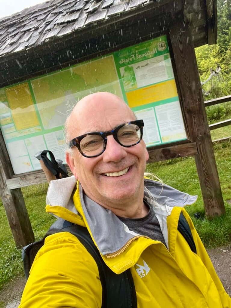 Hiker in yellow rain jacket smiling at Grayson Highlands trailhead on a rainy day.