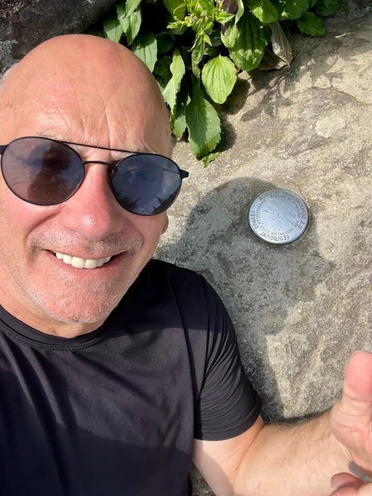 Hiker smiling beside the Clingmans Dome summit marker in Great Smoky Mountains National Park