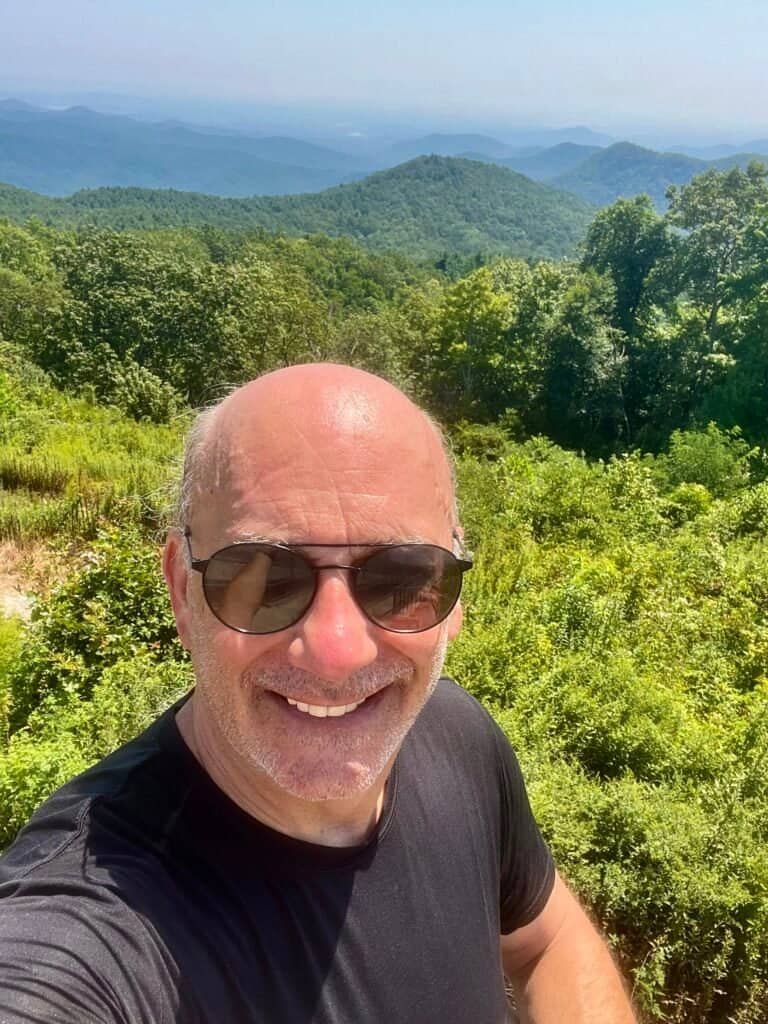 Hiker selfie at the summit of Sassafras Mountain with Blue Ridge Mountain views in the background