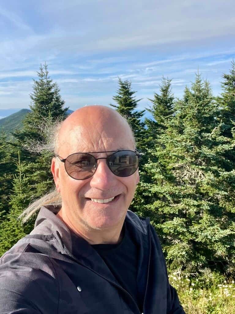 Smiling summit selfie at Mount Mitchell with evergreen forest and blue sky in the background
