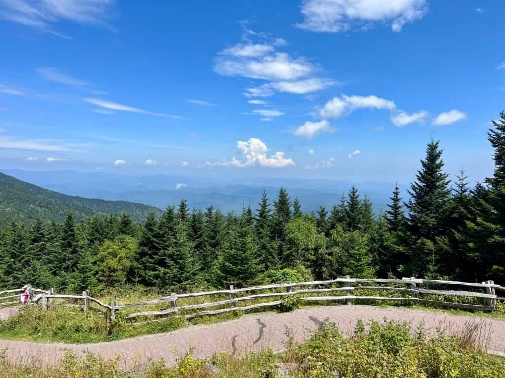 Paved summit path and wooden fence overlooking layered Blue Ridge Mountains under a clear blue sky