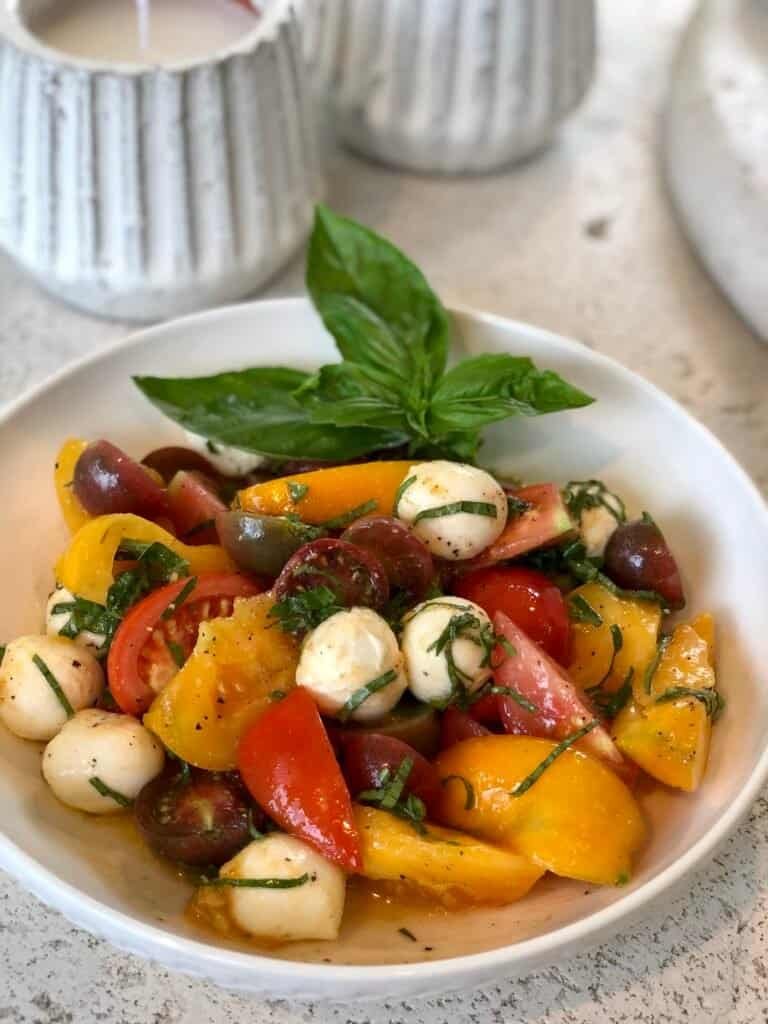 Caprese salad made with homegrown heirloom tomatoes, fresh basil, and mozzarella pearls drizzled with olive oil