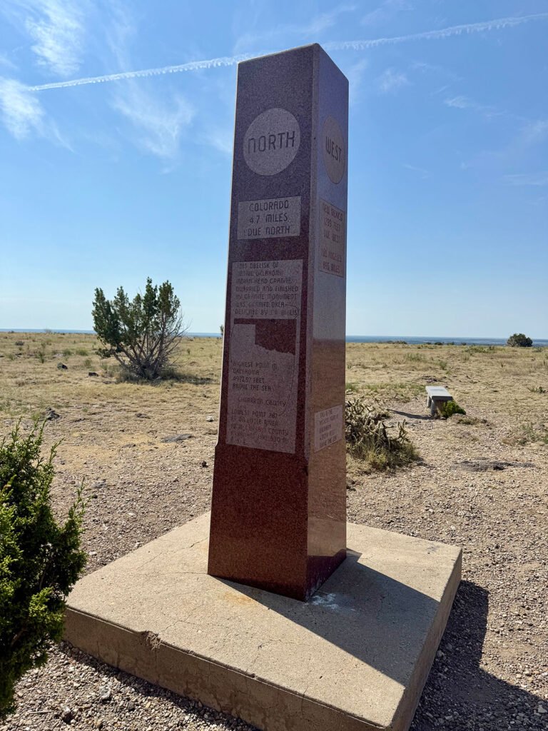The “North” and “West” sides of the summit obelisk, showing Colorado’s distance due north, with desert vegetation and open horizon in the background.