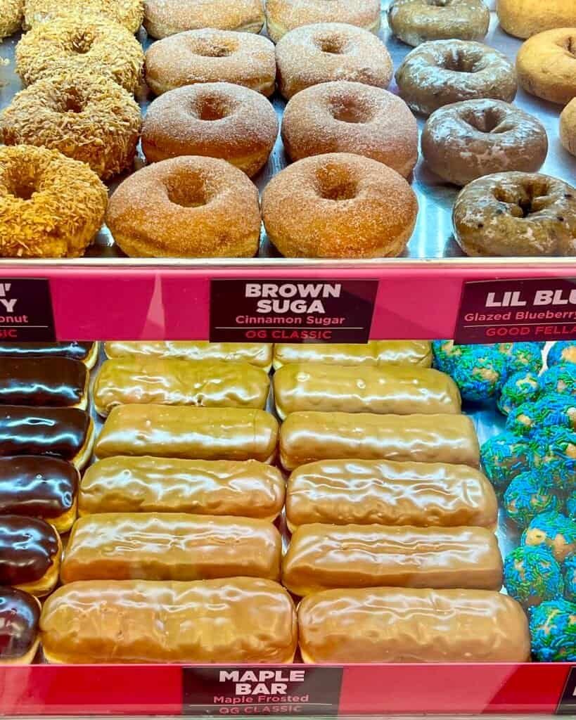 Classic doughnuts including brown sugar rings and maple bars lined up in a bakery display case.