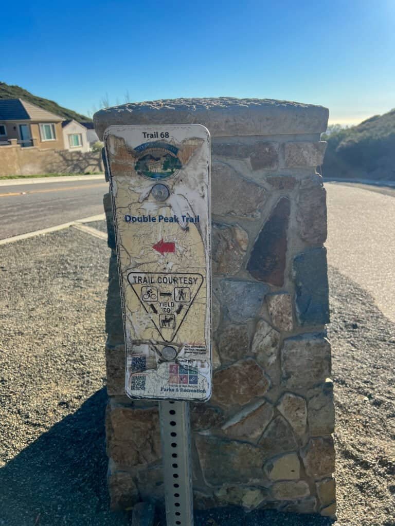 Weathered Double Peak Trail sign (Trail 68) mounted on a stone pillar near Double Peak Drive in San Marcos, California.