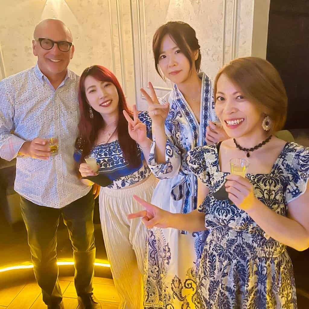 Four people smiling and holding drinks backstage with band members after a live jazz performance.