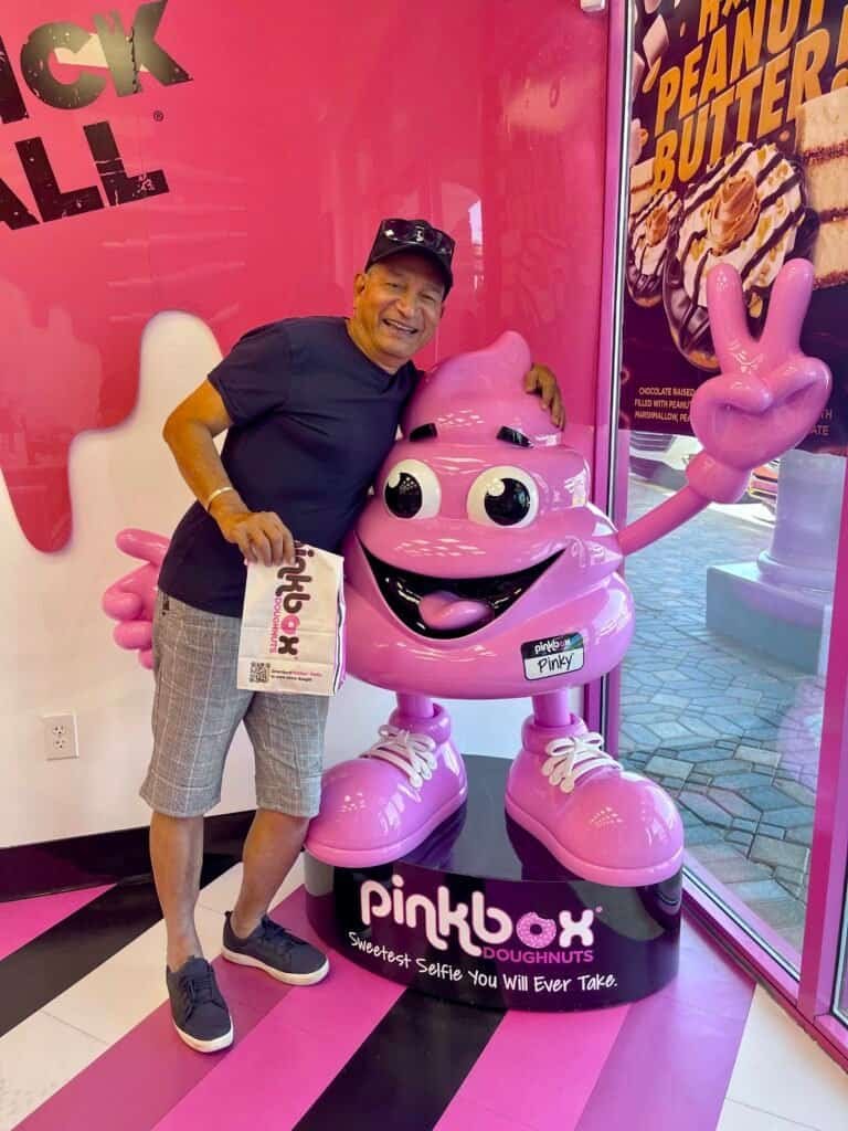 Man posing with the Pinky mascot statue inside Pinkbox Doughnuts in Las Vegas.