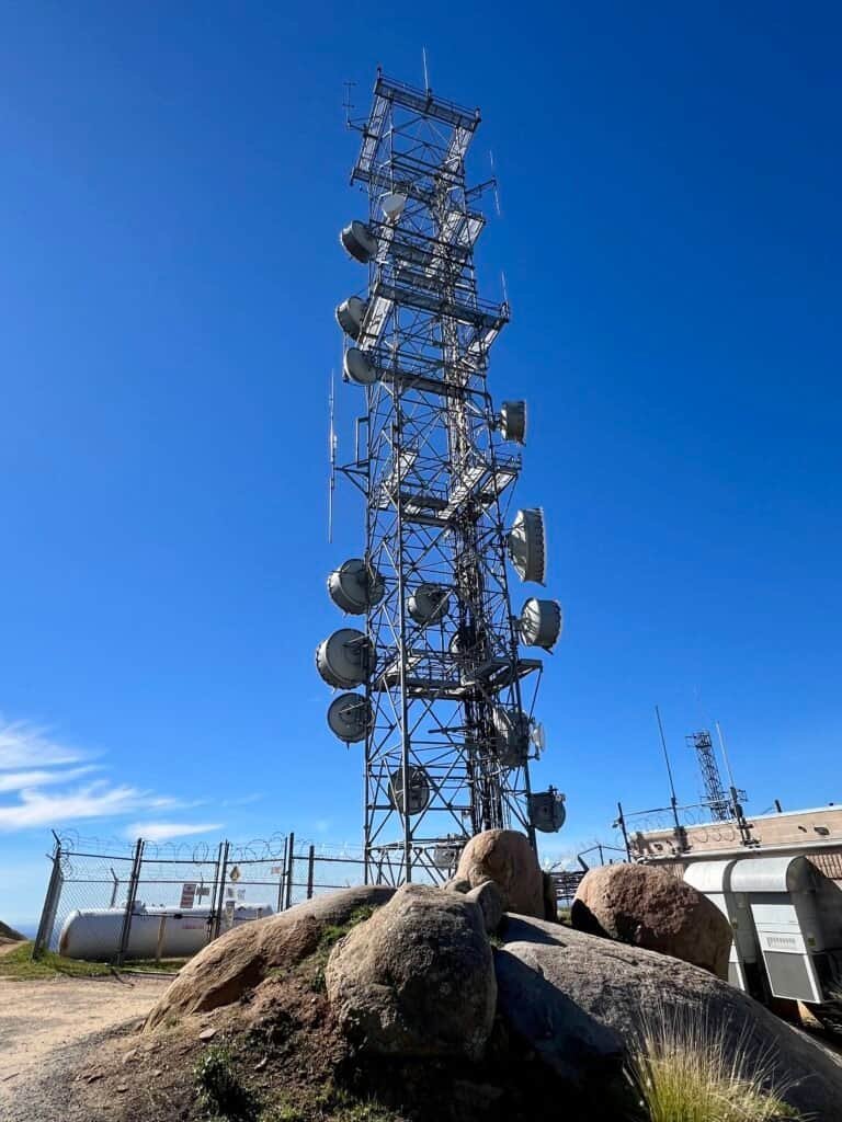 A tall communication tower equipped with antennas and satellite dishes against a bright blue sky atmosphere.
