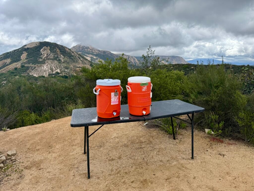 Home Depot water coolers set out on a table along the El Cajon Mountain trail, offering emergency water for hikers.