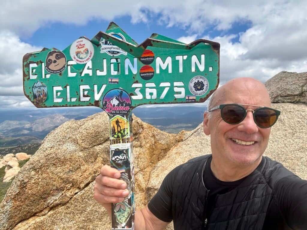 Hiker smiling beside the El Cajon Mountain summit sign at 3,675 feet elevation.