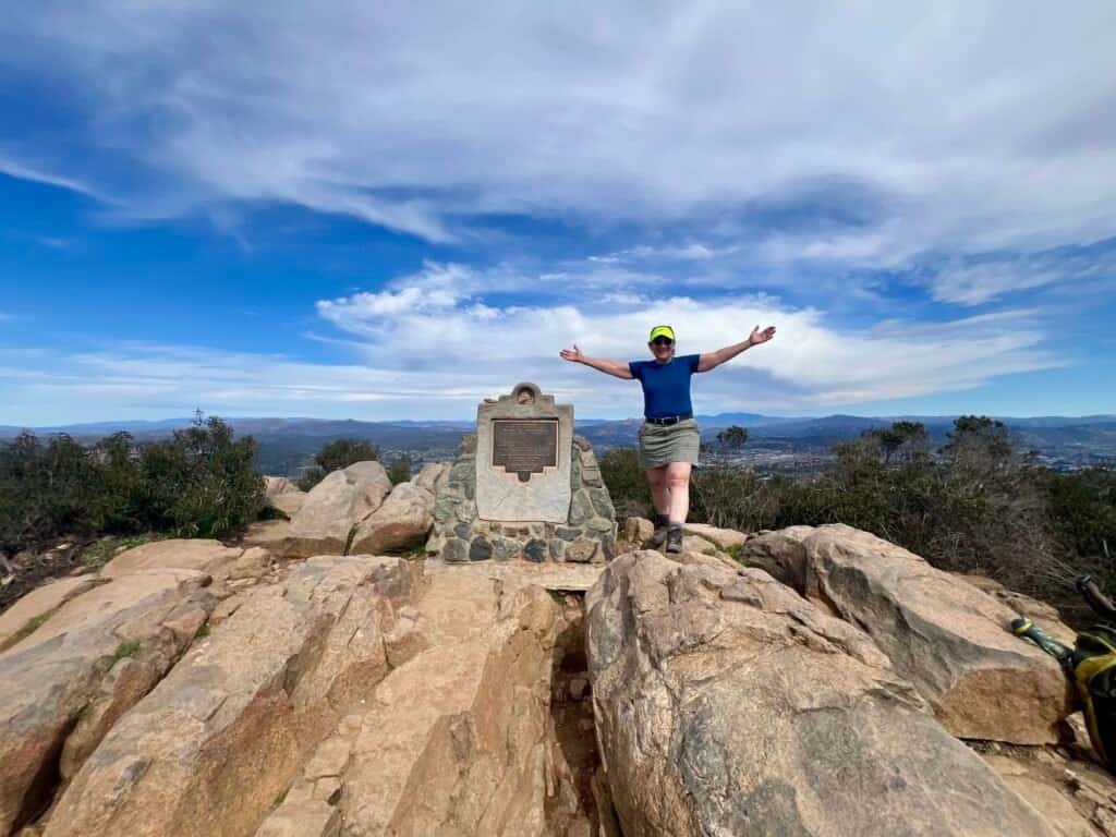 Hiker standing at the Cowles Mountain summit beside the summit marker