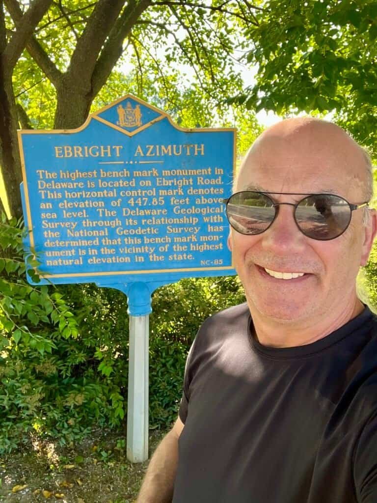Visitor standing beside the Ebright Azimuth historical marker marking Delaware’s highest point