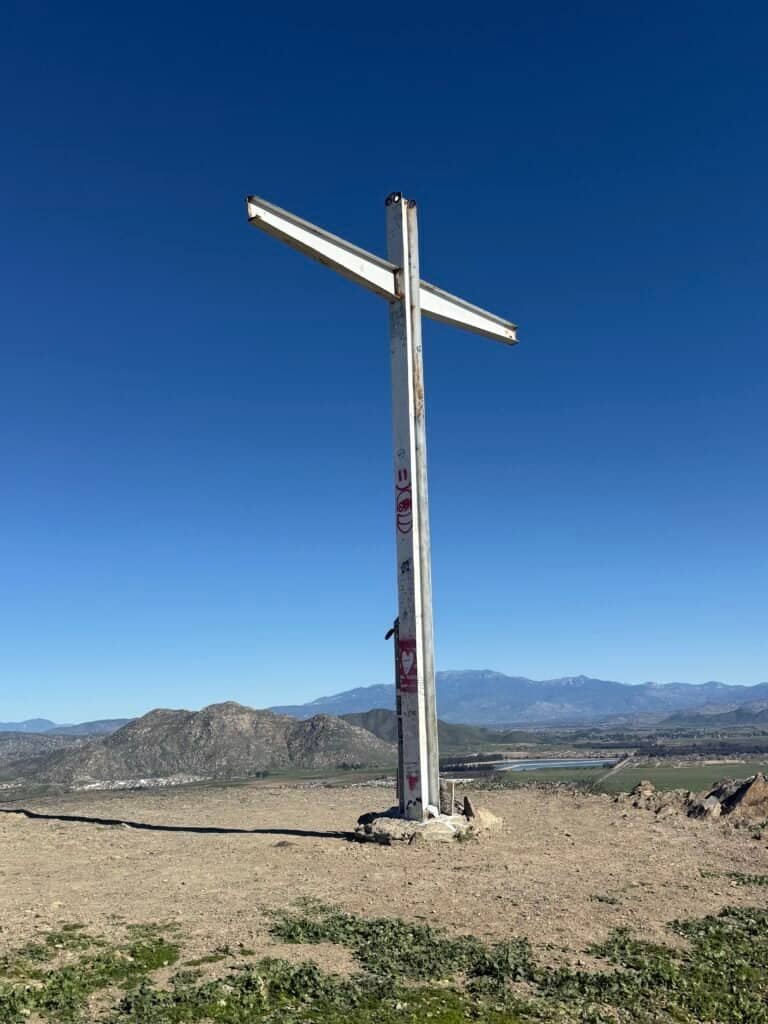 Metal cross marking the first summit of the Three Peaks Loop with valley and mountains below