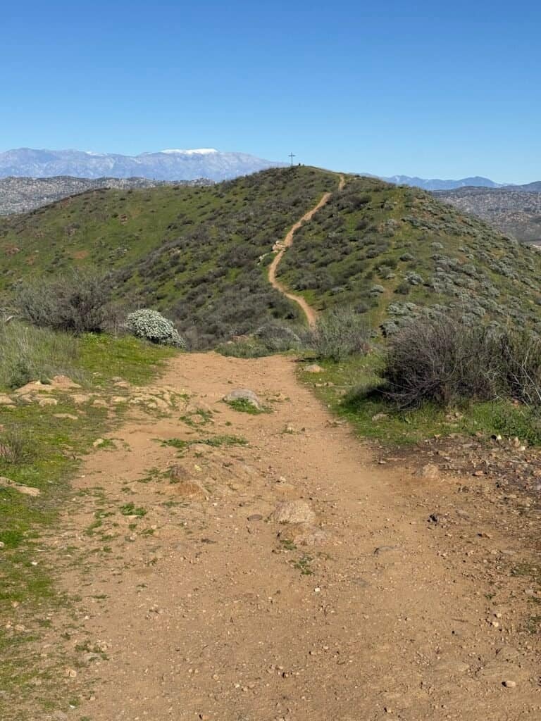 View from the plateau showing the descent and final uphill climb to the third summit, marked by a cross on the ridgeline.