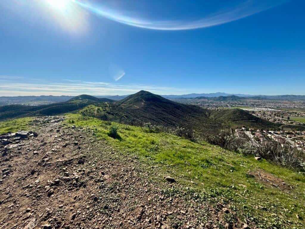 View from the third summit looking back toward the second summit, with a narrow ridgeline trail and rolling green hills below