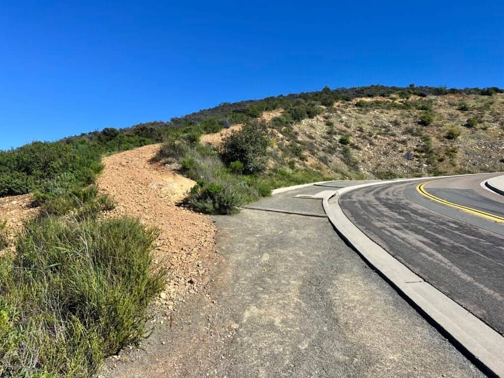Dirt trail climbing alongside Double Peak Drive, showing the final uphill approach toward Double Peak summit in San Marcos