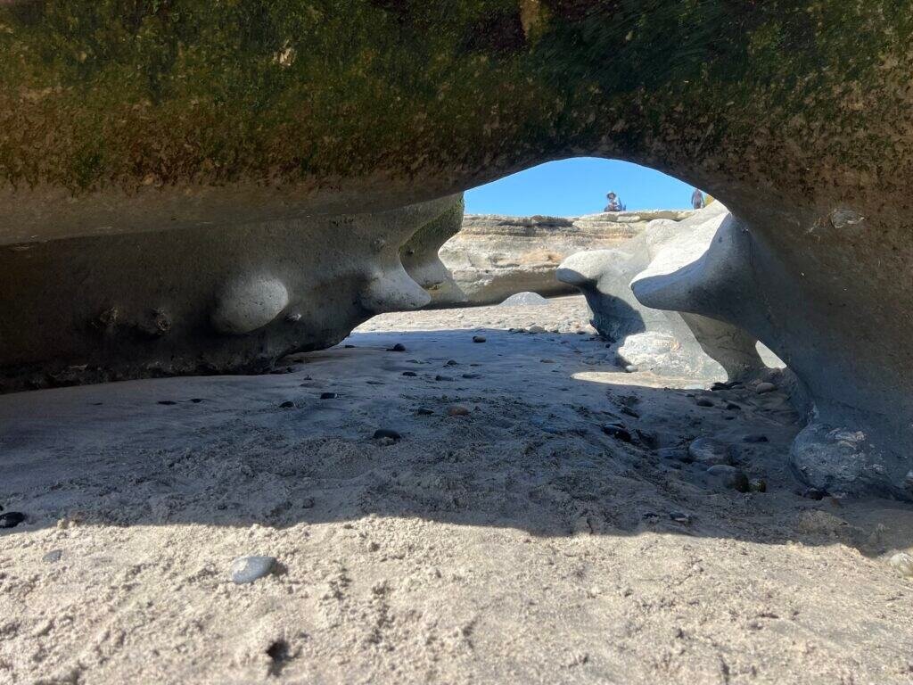Low-tide rock arch framing the beach, with sculpted stone and sand beneath.