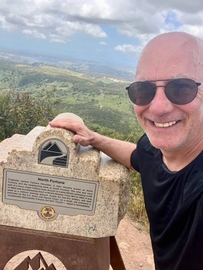 Hiker at the North Fortuna summit beside the official marker with views across Mission Trails