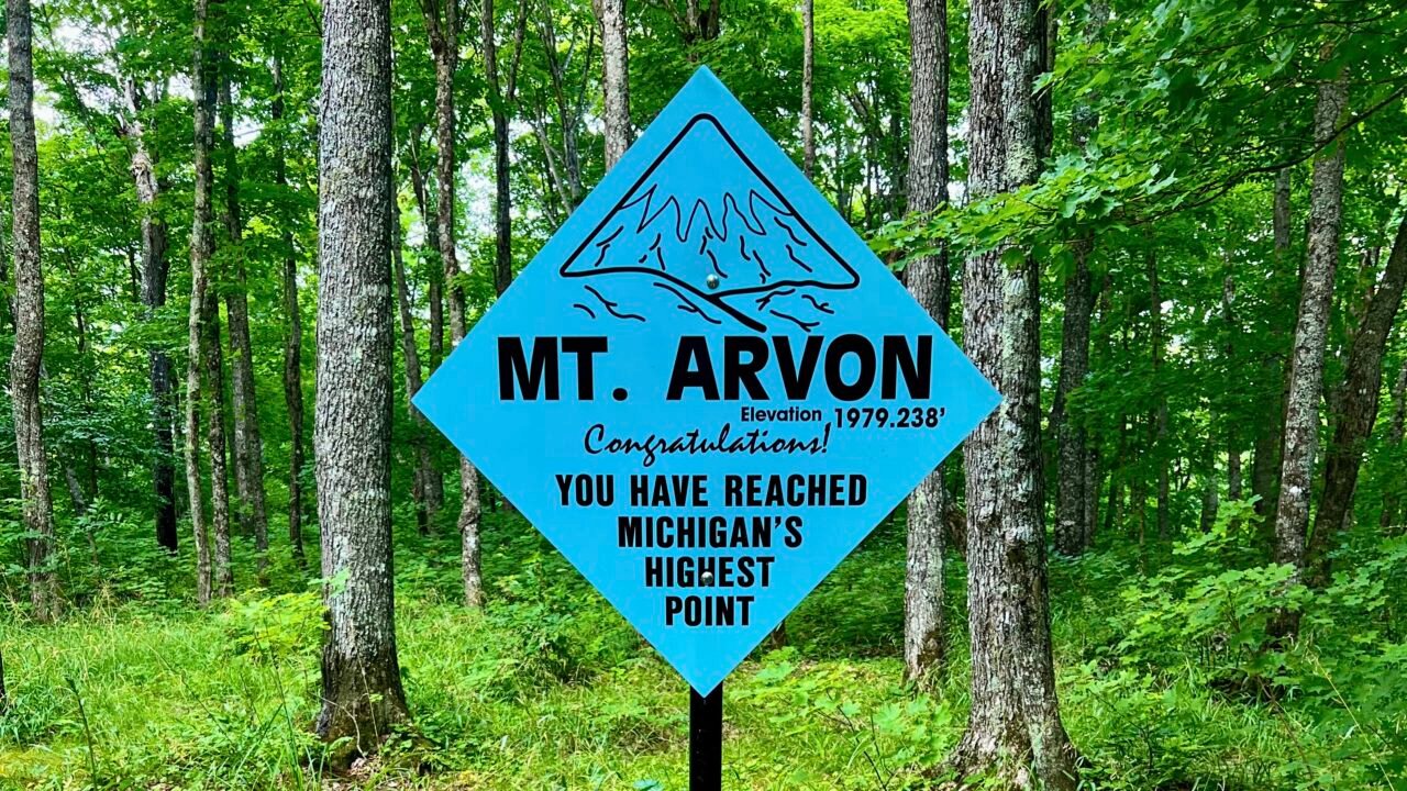 Blue “Mt. Arvon” summit sign marking Michigan’s highest point at 1,979 feet in a wooded Upper Peninsula forest.