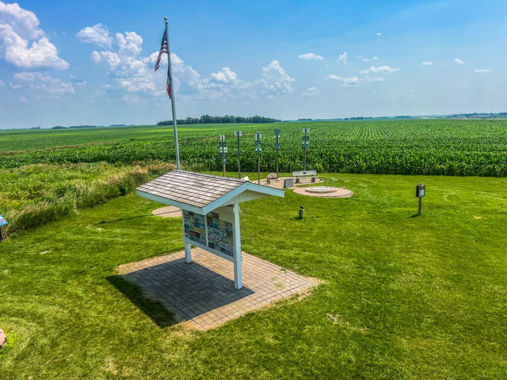 View from the Hawkeye Point silo observation deck overlooking the summit mosaic, flagpole, and expansive Iowa cornfields.