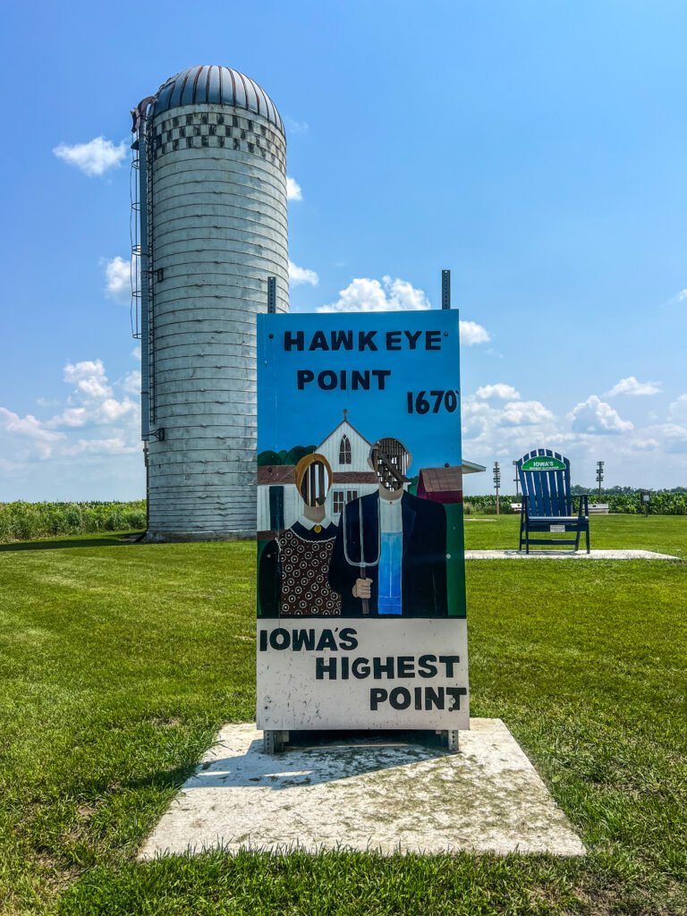 American Gothic-themed photo cut-out board at Hawkeye Point with silo and Iowa’s highest point sign in the background.
