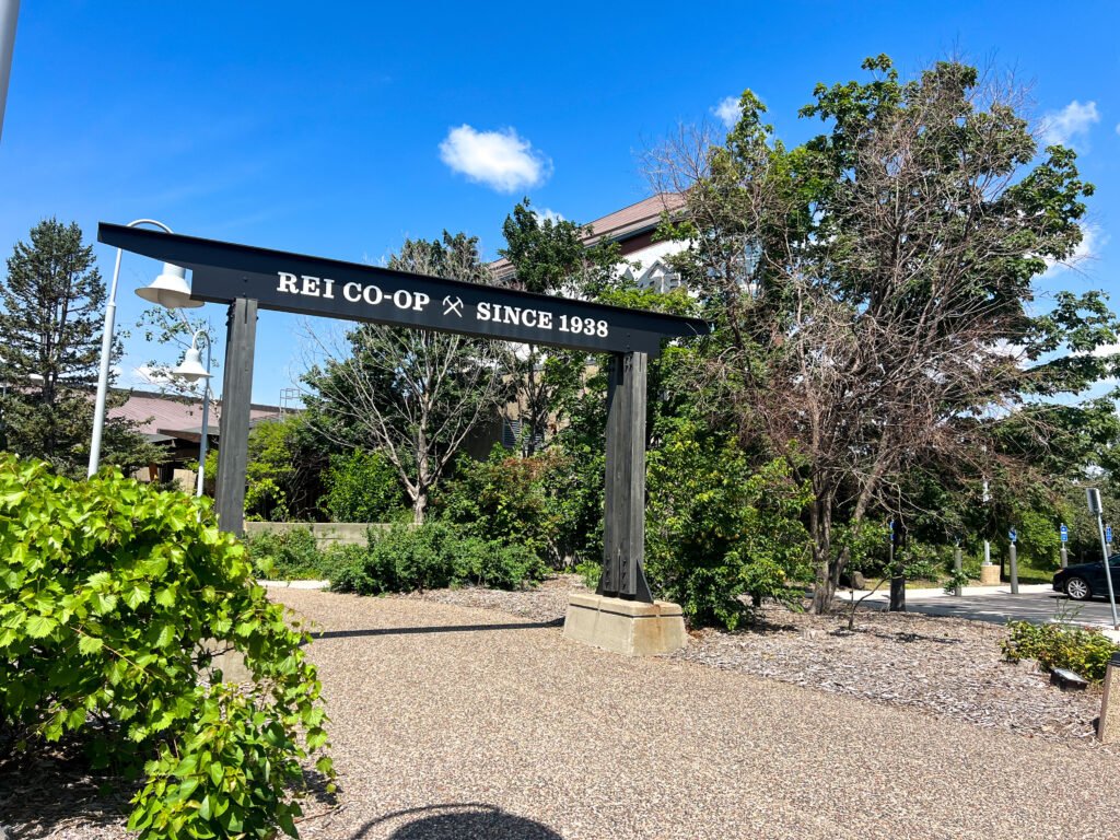 REI Co-op flagship store entrance sign in Bloomington, Minnesota under a bright blue sky.