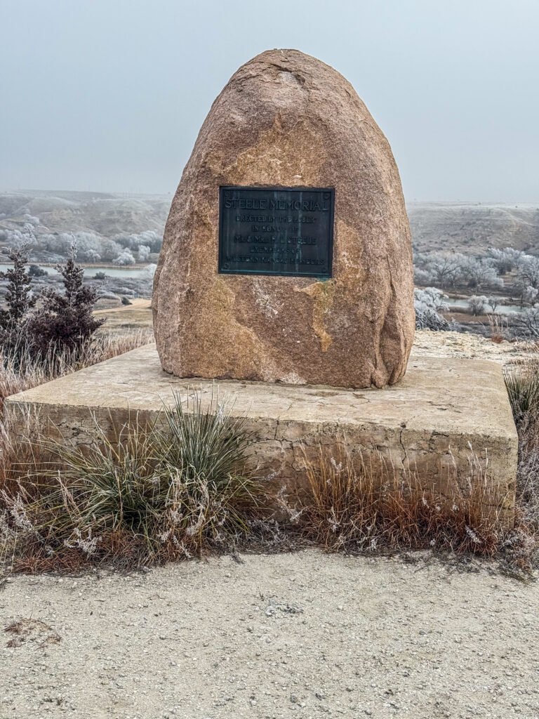 Steele Memorial monument overlooking Lake Scott valley, a large stone marker with plaque set against a frosty prairie landscape.