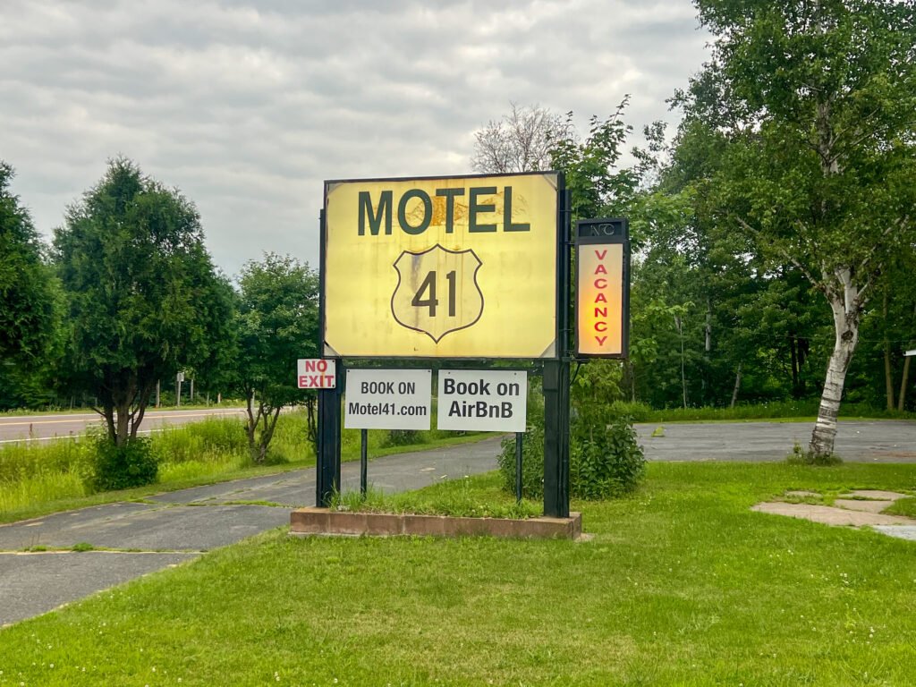 Roadside Motel 41 sign in L’Anse, Michigan advertising vacancy and Airbnb booking along a wooded Upper Peninsula highway.