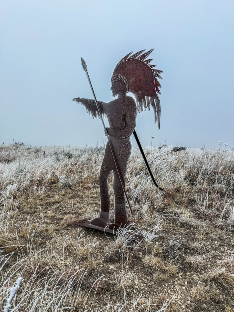 Metal statue of a Native American figure with spear standing on a bluff above Lake Scott in Kansas.