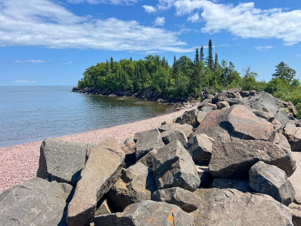 Rocky shoreline and breakwater leading toward Artist Point along Lake Superior under a blue sky