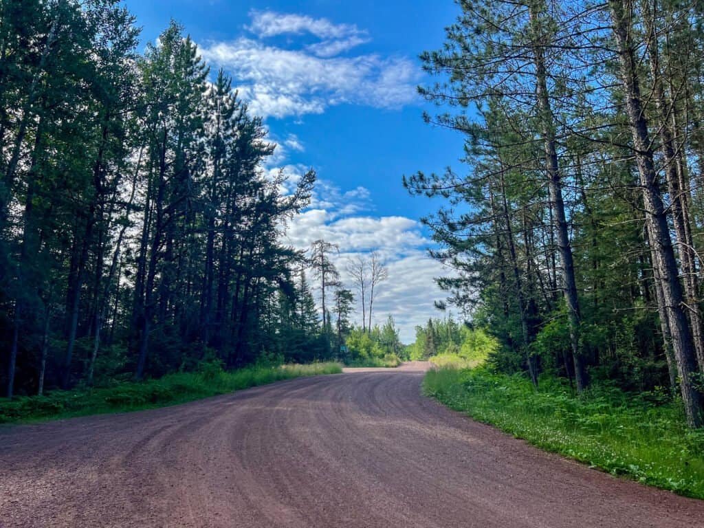 Gravel forest road leading toward the Eagle Mountain trailhead through dense pine forest in northeastern Minnesota.