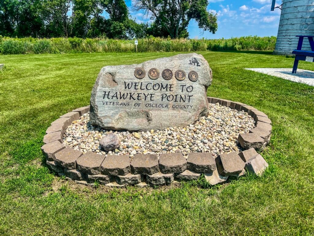 Stone welcome marker at Hawkeye Point honoring Osceola County veterans surrounded by grass and landscaping.
