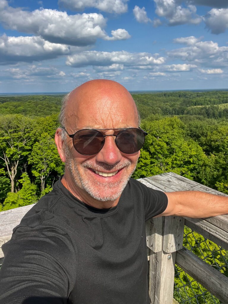 Smiling summit selfie at the top of Timms Hill observation tower with forest views behind