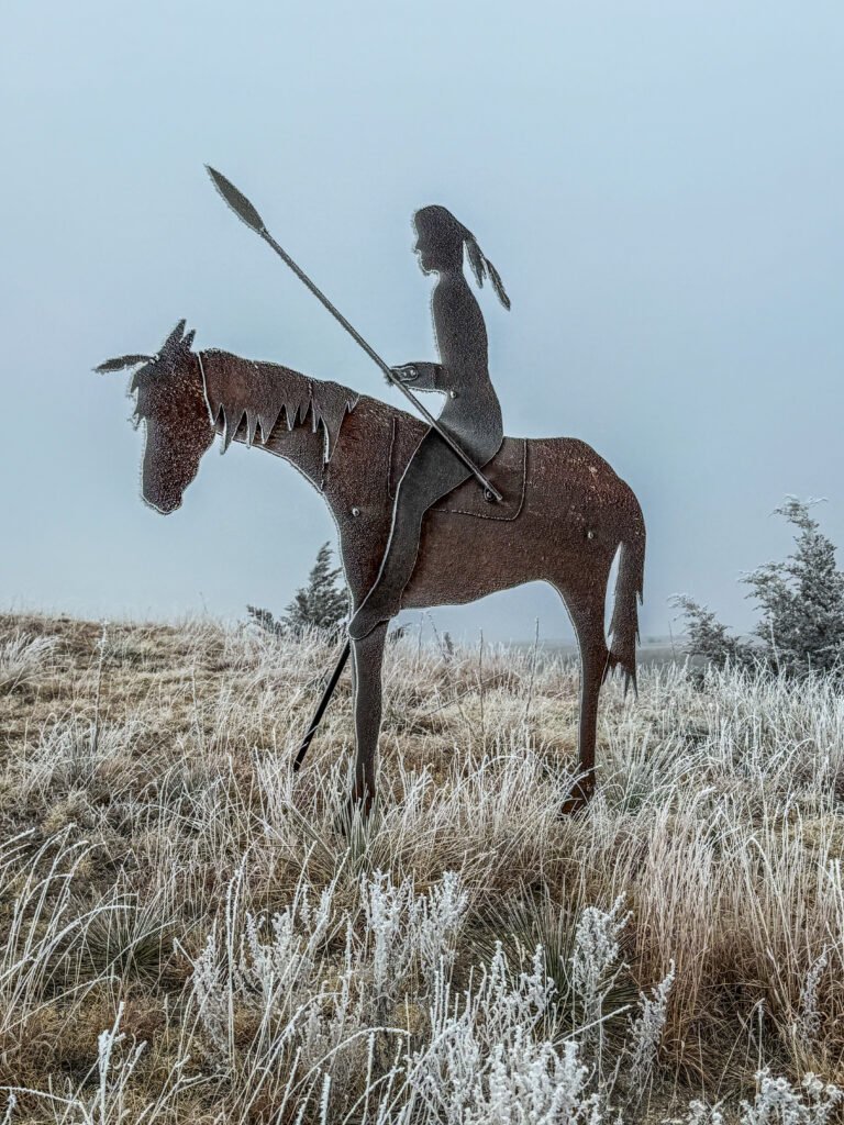 Metal statue of a Native American rider on horseback overlooking frost-covered prairie at Lake Scott in winter.