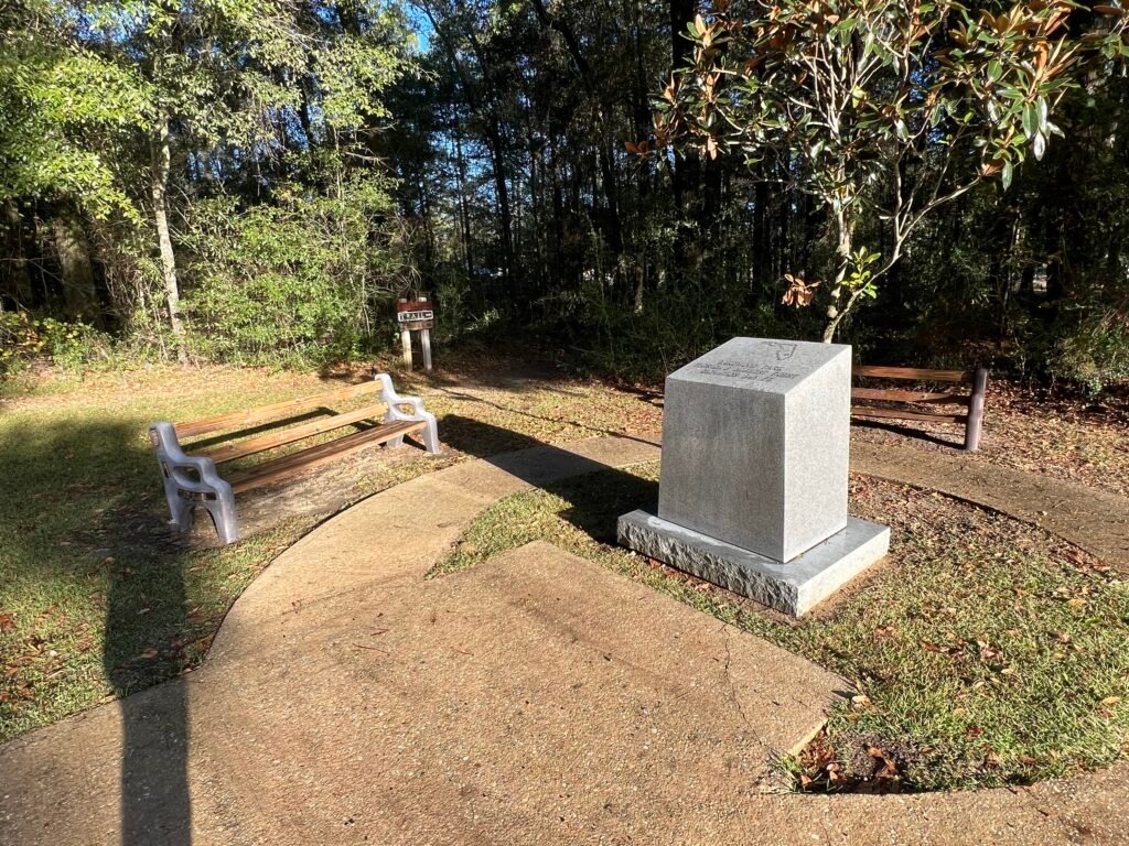 Summit area at Britton Hill in Lakewood Park with granite high point marker, benches, and trailhead sign in the background.